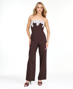 A woman modeling a dark brown pinstriped strapless jumpsuit with a white floral lace bodice trim, photographed against a plain white studio background.