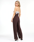 A woman modeling a dark brown pinstriped strapless jumpsuit with a white floral lace bodice trim, photographed against a plain white studio background.