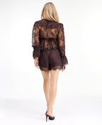 A model wearing dark brown lace shorts with a drawstring waist and lace trim edges, paired with matching brown heeled sandals and a matching top, against a plain white studio background.