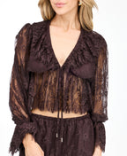 A model wearing dark brown lace shorts with a drawstring waist and lace trim edges, paired with matching brown heeled sandals and a matching top, against a plain white studio background.