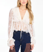 A woman modeling a white lace long-sleeve top with a deep V-neck and ruffled hem and matching shorts, paired with brown suede knee-high boots, against a plain white studio background.