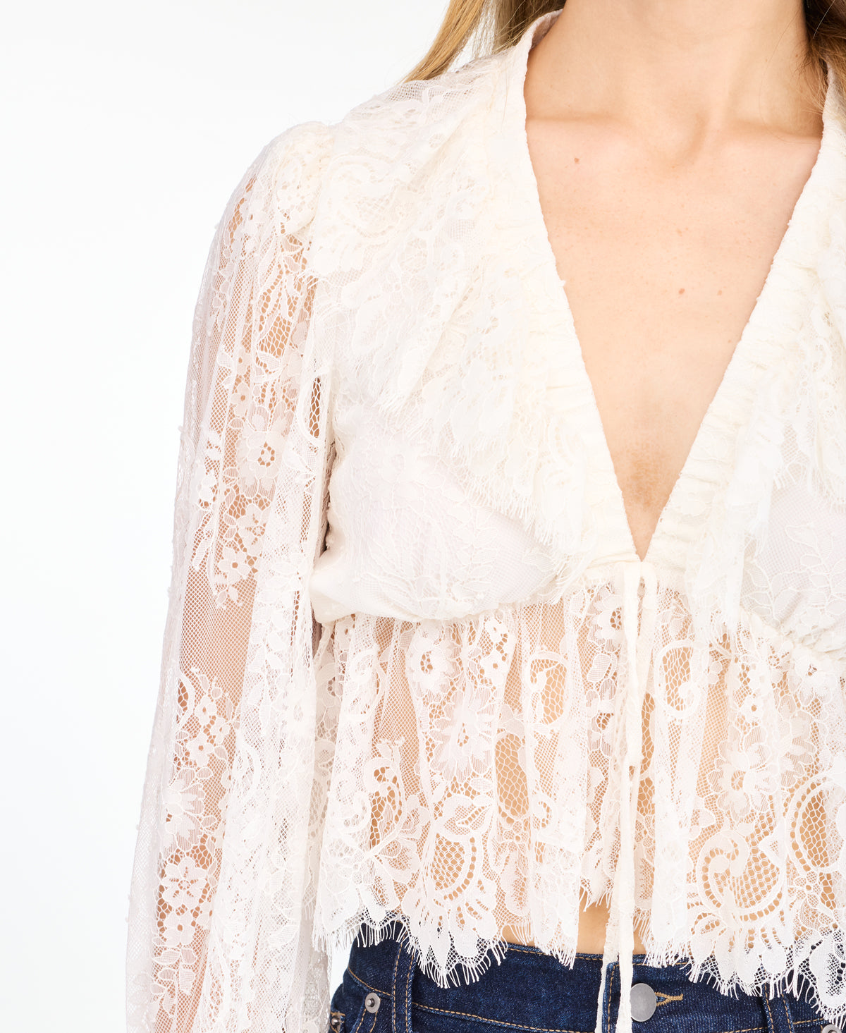 A woman modeling a white lace long-sleeve top with a deep V-neck and ruffled hem and matching shorts, paired with brown suede knee-high boots, against a plain white studio background.