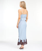 Model wearing a blue satin tank with chocolate brown embroidered appliqué and a matching midi skirt standing against a white background