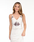 A woman modeling a white tank with matching midi skirt with dark brown floral lace on the bodice and hem, set against a plain white studio background.