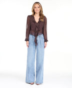 Model wearing a brown chiffon polka dot top with a removable neck scarf, medium wash denim jeans, and brown kitten heels