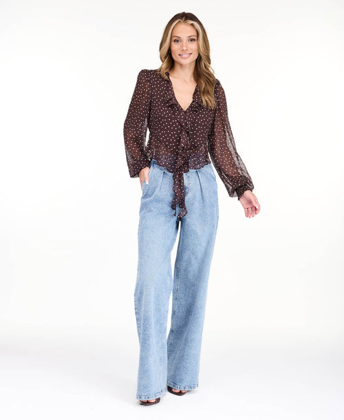 Model wearing a brown chiffon polka dot top with a removable neck scarf, medium wash denim jeans, and brown kitten heels