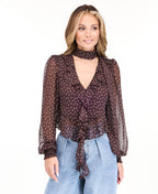 Model wearing a brown chiffon polka dot top with a removable neck scarf, medium wash denim jeans, and brown kitten heels