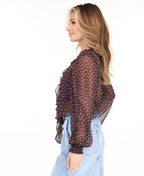 Model wearing a brown chiffon polka dot top with a removable neck scarf, medium wash denim jeans, and brown kitten heels