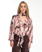 Model wearing a pink snake print top with brown suede pants and brown kitten heels standing against a white back drop