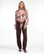 Model wearing a pink snake print top with brown suede pants and brown kitten heels standing against a white back drop