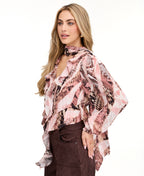 Model wearing a pink snake print top with brown suede pants and brown kitten heels standing against a white back drop