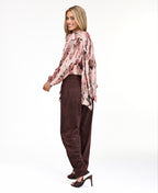 Model wearing a pink snake print top with brown suede pants and brown kitten heels standing against a white back drop
