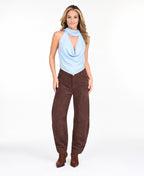 Model wearing a blue cowl neck tank with a removable neck scarf paired with brown sueded pants standing on a white background