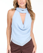 Model wearing a blue cowl neck tank with a removable neck scarf paired with brown sueded pants standing on a white background