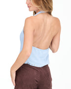Model wearing a blue cowl neck tank with a removable neck scarf paired with brown sueded pants standing on a white background