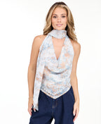 A woman modeling a light blue sleeveless halter top with a textured pattern and removable scarf  and light-wash wide-leg denim pants against a plain white studio background.