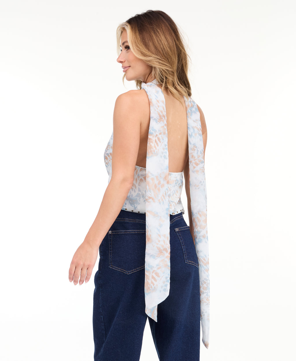 A woman modeling a light blue sleeveless halter top with a textured pattern and removable scarf  and light-wash wide-leg denim pants against a plain white studio background.