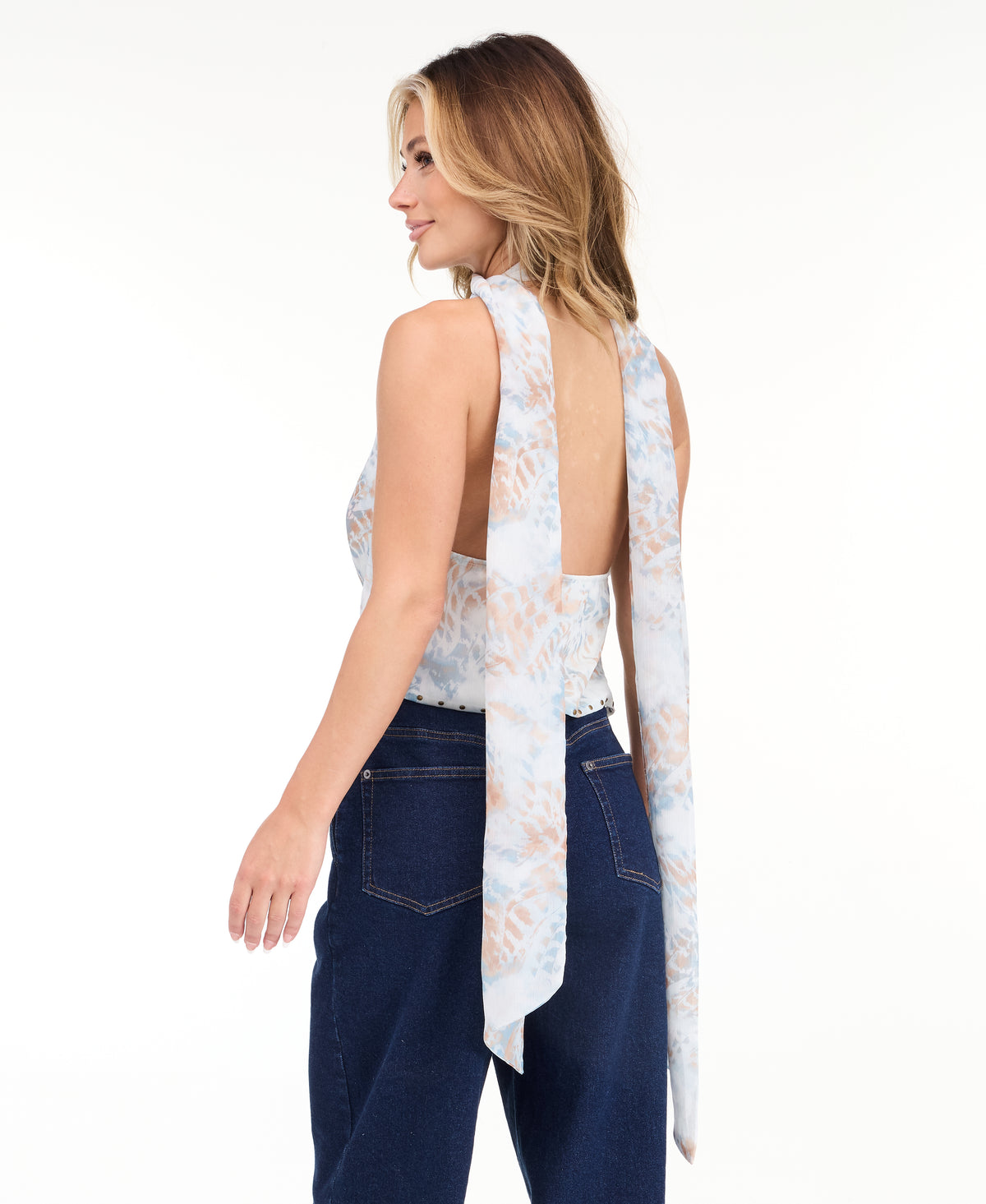 A woman modeling a light blue sleeveless halter top with a textured pattern and removable scarf  and light-wash wide-leg denim pants against a plain white studio background.
