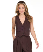 A woman modeling a dark brown pinstriped sleeveless vest-style top and barrel pants, standing against a plain white studio background.
