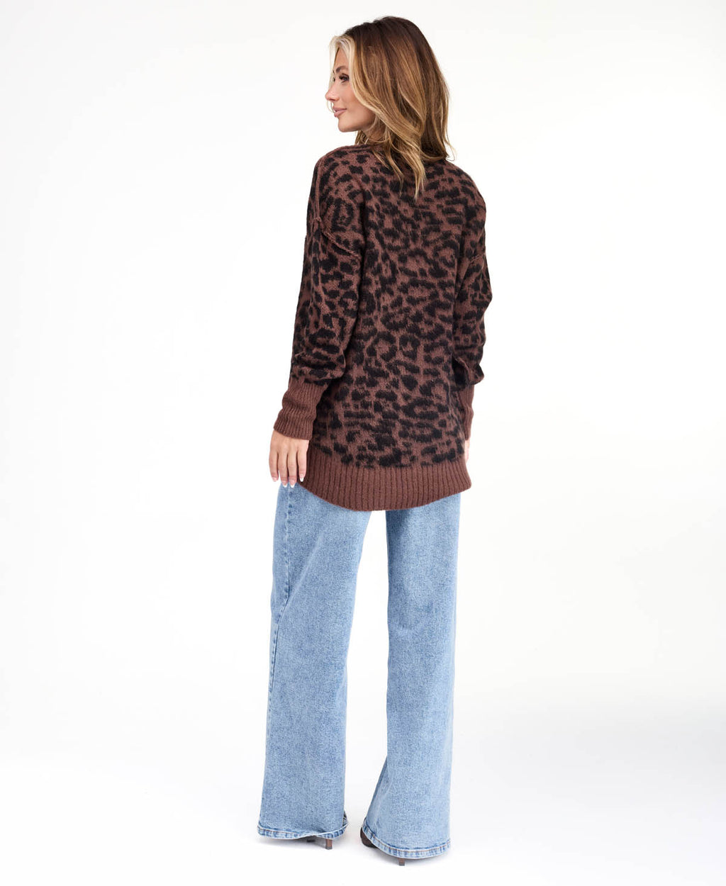 Model wearing an oversized  cheetah crew neck sweater with medium wash denim jeans.
