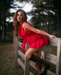 Jessie in a red skirt and top and brown boots leaning against a wooden fence