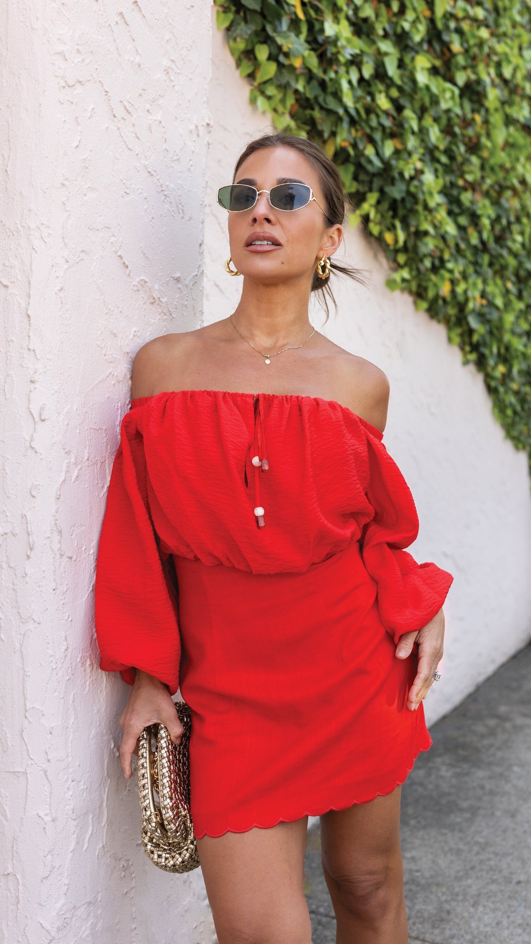 Jessie in red outfit leaning against an ivy wall. 