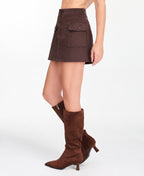 A model wearing a brown suede mini skirt with button and scallop details and matching brown knee-high boots, shown from the waist down on a white studio background.