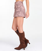 Model wearing a pink snake print skirt with a matching bomber jacket, styled with brown knee high boots. 