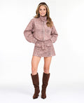 Model wearing a pink snake print skirt with a matching bomber jacket, styled with brown knee high boots. 