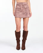 Model wearing a pink snake print skirt with a matching bomber jacket, styled with brown knee high boots. 