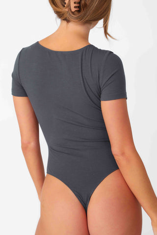 Model wearing Charcoal Ribbed Short Sleeve Bodysuit, stretchy rib knit seamless fabrication, with scoop neckline and thong coverage.