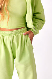 Front view of model wearing green KiKi Joggers with hands in pockets, paired with matching KiKi full zip and razorback tank.
