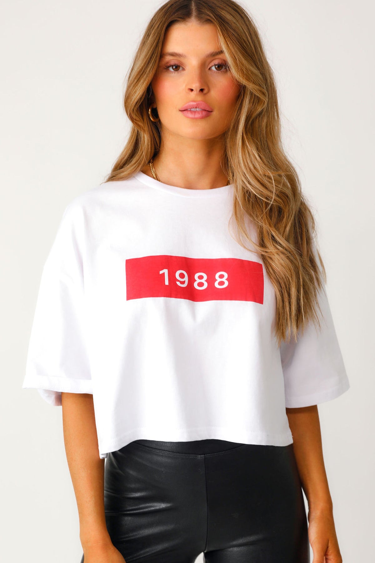 Close up front view of model wearing white and red '1988' cropped tee with 'Bet On Me' black faux leather leggings.