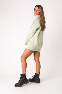 Full body side view of model wearing the lime green 'Lean On Me' quarter zip sweater, shown as a dress paired with combat boots. 