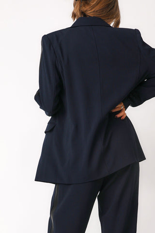 Close up back view of model wearing 'Bianca' navy blazer show casing center back seam, shoulder pads, and classic collar detail. Paired with 'Bianca' navy trousers.