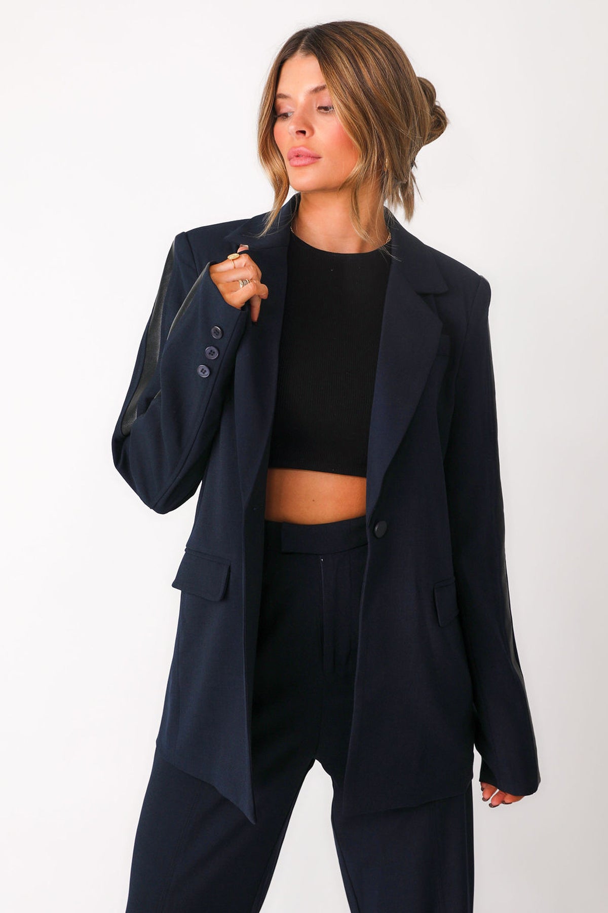 Close up front view of model wearing 'Bianca' navy trousers with faux black leather paneling detail down outer seam of sleeves, paired with matching 'Bianca' navy blazer worn open over black basics bra tank.