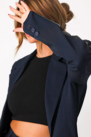 Close up front view of modeling wearing 'Bianca' navy blazer show casing 3 button detail at cuff , and  notch lapel. Paired with black basics bra tank. 