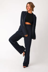 Full body front view of  model wearing 'Bianca' navy trousers with faux black leather paneling detail down outer seam of sleeves, paired with matching 'Bianca' navy blazer worn open over black basics bra tank.
