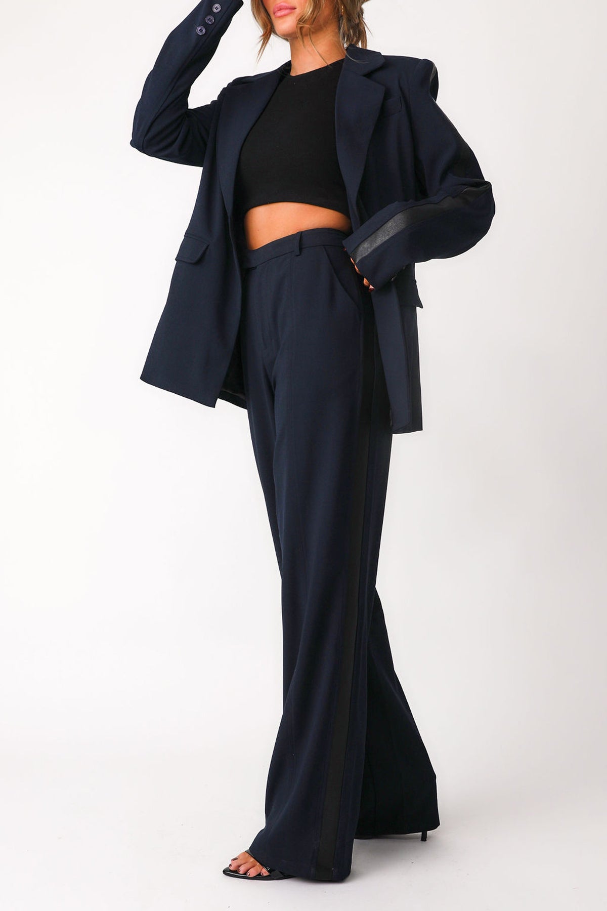 Full body front view of model model wearing 'Bianca' navy trousers paired with matching 'Bianca' navy blazer worn open over black basics bra tank.