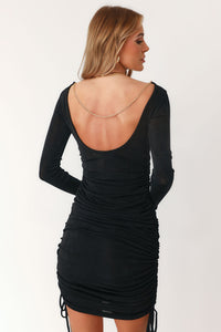 Model wearing Black Multi Functional Dress with Fully Adjustable Length Strings on Each Side Seam. Front Boat Neckline,  Gold Chain Draped Across Back,  Long Sleeves 