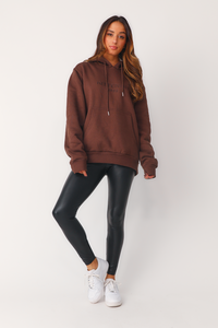 Full body front view of model wearing 'Bet On Me' back faux leather leggings, paired with the 'Chocolate Kittenish Logo' sweatshirt and white sneakers. 